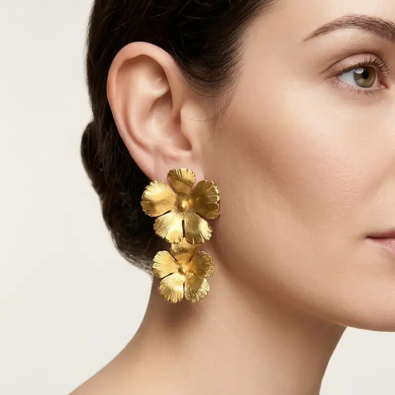 Close-up beauty shot of a gold flower drop earring worn on a model's ear, tight crop showing both fit and metal detail