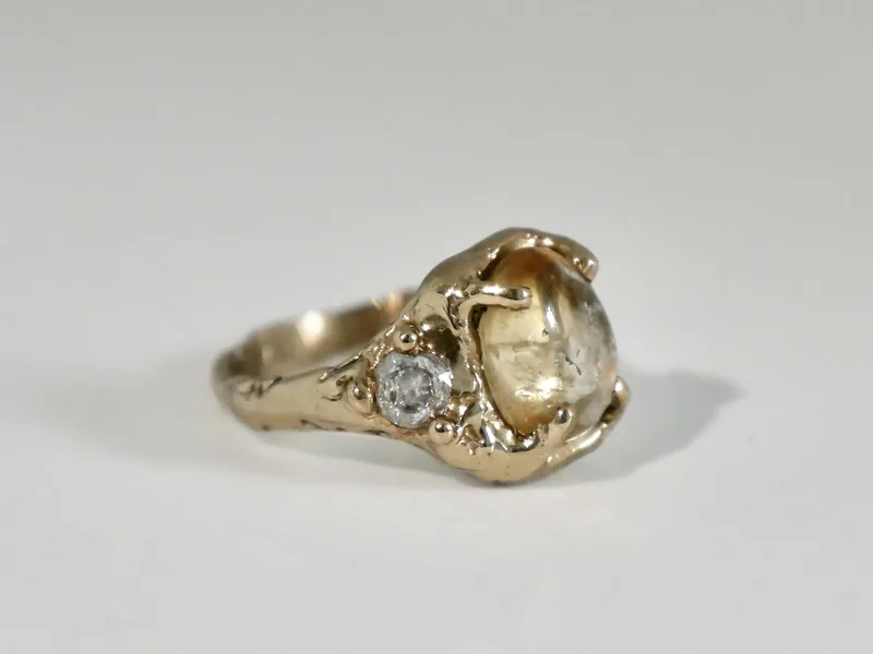 An antique gold ring with a pale cabochon stone and a single diamond accent, photographed alone on a plain grey studio backdrop