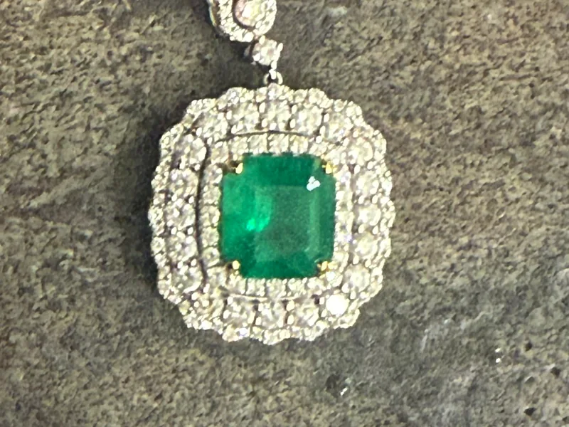 The original phone photo of the emerald and diamond pendant on a rough stone slab