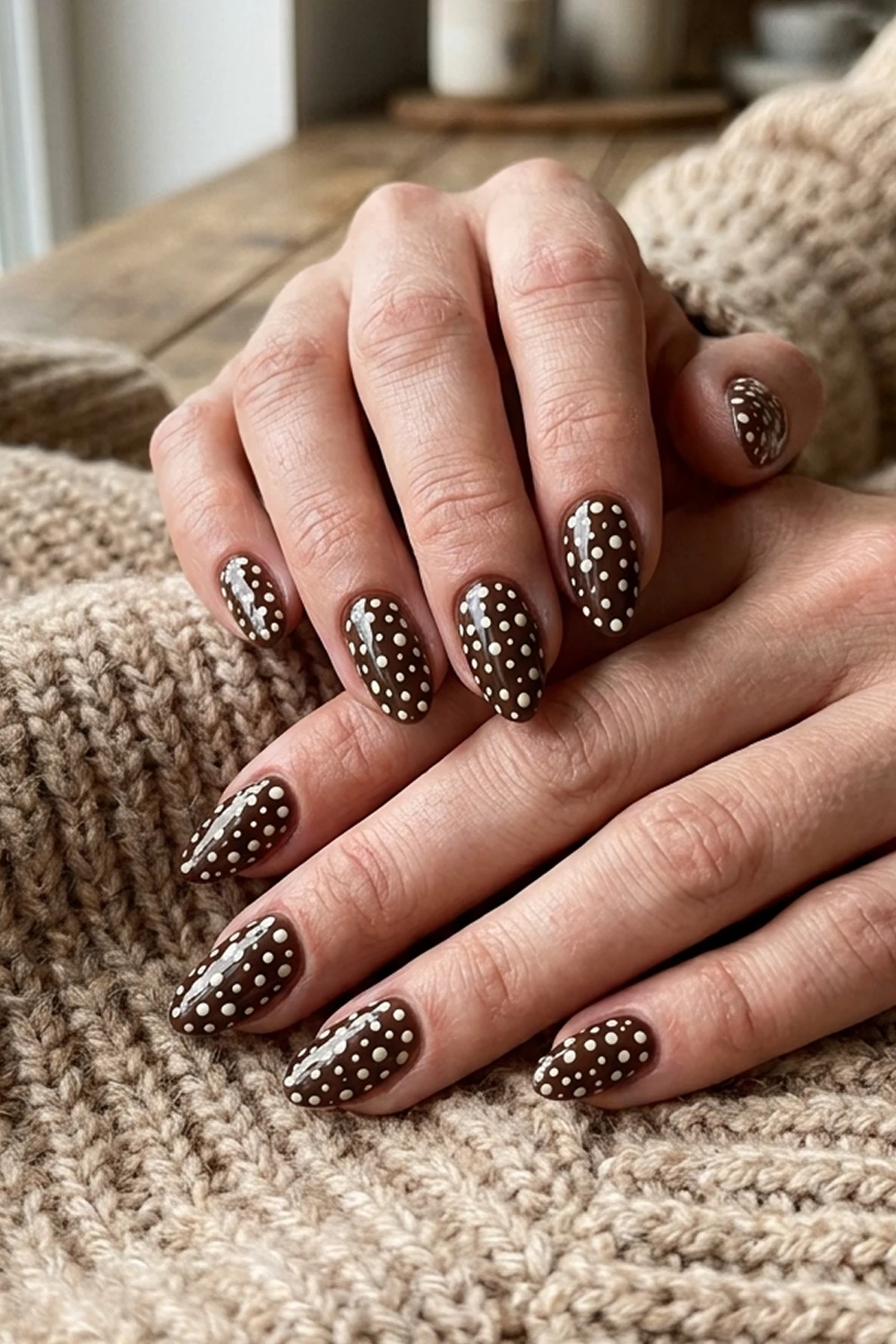 Espresso brown polka dot almond nails — trending early fall nails 2026 design shown on hands resting on a chunky beige knit sweater