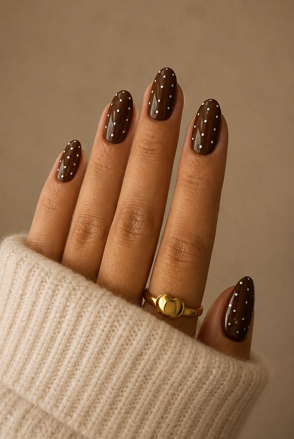 Chocolate brown polka dot almond nails — trending Summer to Fall Transition Nails design shown on a hand in a cream knit sweater