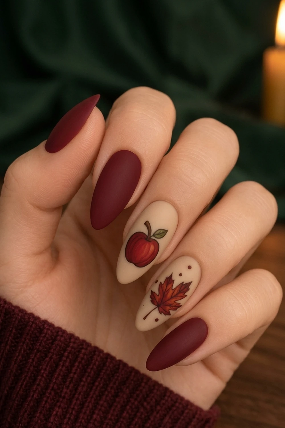 Burgundy apple & maple fall nails 2026 — matte almond design shown on a hand with candle backdrop
