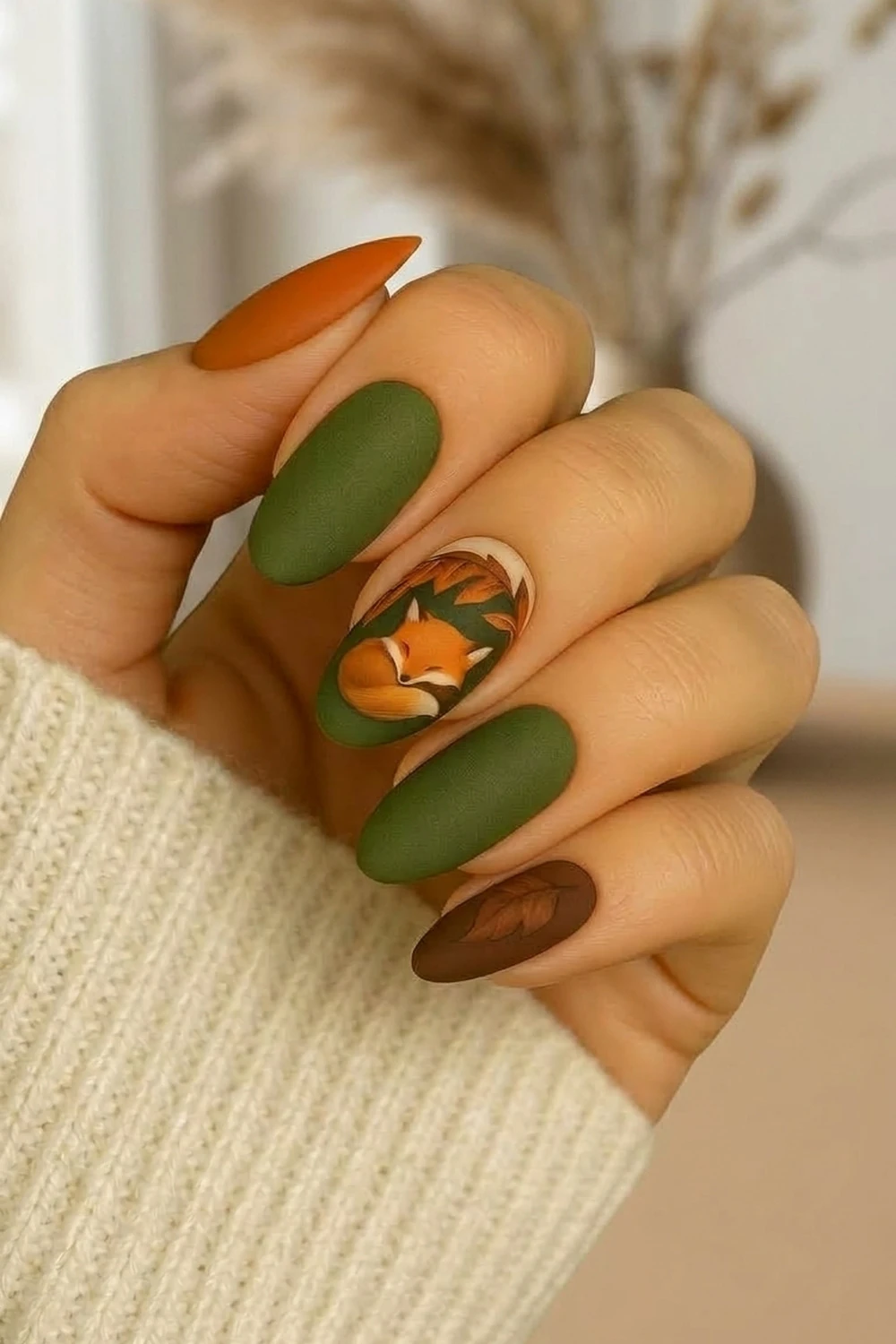 Fox & leaf fall acrylic nails — matte olive and brown almond design shown on a hand with pampas backdrop